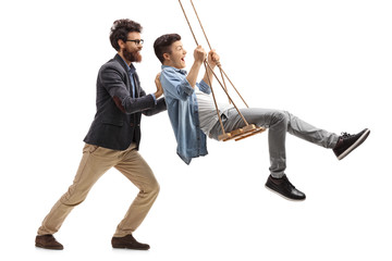 Father pushing his teenage son on a wooden swing - obrazy, fototapety, plakaty