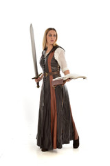 full length portrait of girl wearing brown  fantasy costume, holding a sword. standing pose on white studio background. 