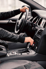 Businessman driving luxury modern car in the city. Close up man's hand on the gearbox.