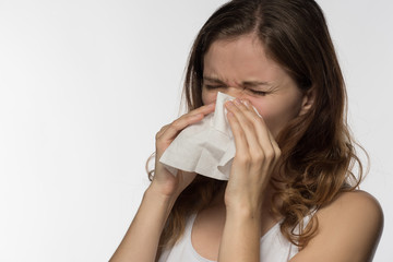 A beautiful brunette woman becomes ill with a cold and runny nose, sneezes and coughs into a white paper kerchief