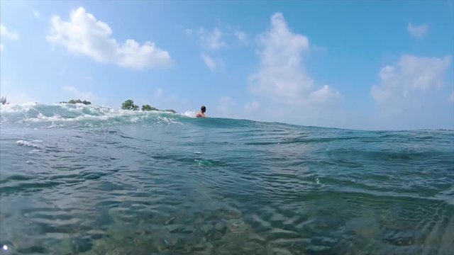 Surfer rides the wave near the camera, smiles and shows the Peace sign into camera. Real speed combined with slow motion