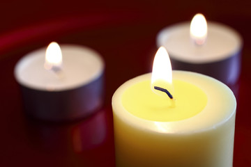 .Close up of a burning wax candle against a red background.
