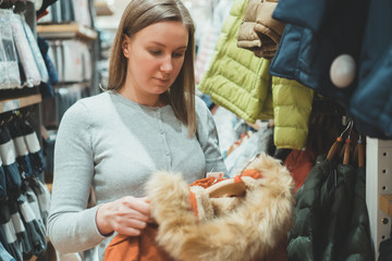 Woman choosing winter jacket with fur in clothing store.