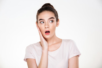 Pretty woman with brown hair in bun touching her face expressing surprise or shock posing isolated over white background