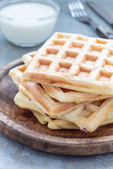 Homemade savory belgian waffles with bacon and shredded cheese, served with plain yogurt, on wooden plate, vertical