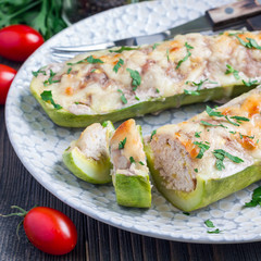 Zucchini boats stuffed with ground meet and topped with cheese on a plate, square format