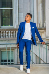 African American college student studying in New York, wearing blue suit, white collarless shirt, sneakers, sitting on railing in vintage office building on campus, taking break, looking up, thinking