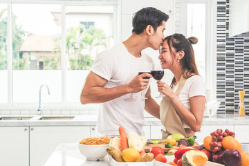 Obraz na płótnie Canvas Asian lovers or couples kissing forehead and drinking wine in kitchen room at home. Love and happiness concept Sweet honeymoon and Valentine day theme