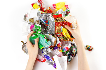 Hands holding a bunch of candy wrappers on a white background. Closeup