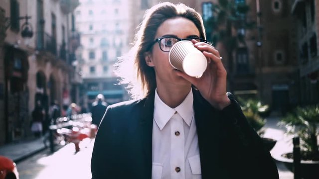 Portrait of young attractive businesswoman drinking coffee to go on a break and using modern smartphone outdoors, sunshine, slow motion