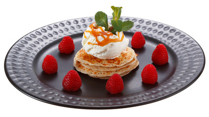 Serving pancakes with ice cream and raspberries on black plate. Decorated with caramel syrup and mint. Isolated on white background.