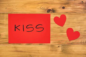Red paper with word kiss and hearts on wooden table.