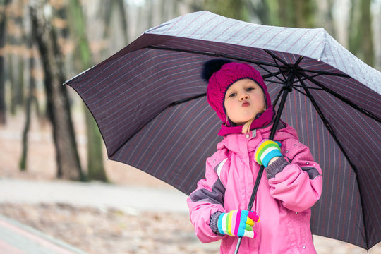 Little  girl walking under umbrella in a city park