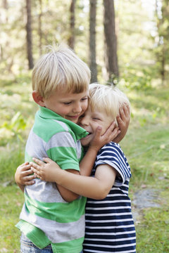 Two blonde boys hugging in forest