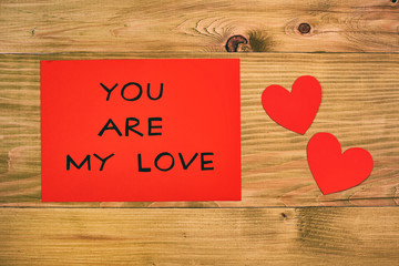 Message you are my love on red paper and hearts on wooden table.