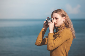 beautiful blonde girl on a sea beach with a old camera in hand