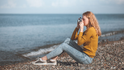 beautiful blonde girl on a sea beach with a old camera in hand