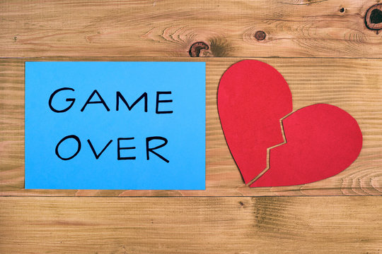 Broken heart and blue paper with text game over on wooden table,relationship breakup concept.