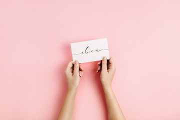 Valentine's Day composition. Female hands holding card with calligraphic quote "I Love U" on pale pink background. Flat lay, top view Love concept.