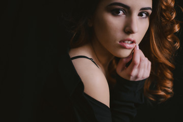 Naklejka premium Beautiful girl with long curly hair, dressed in a black dress, posing on black background. Fashion style and poses