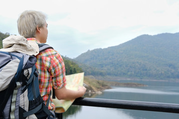 Fototapeta premium traveler man with map, backpack travel at mountain & lake in summer. tourist backpacker relaxing outdoor. hiking lifestyle, vacation concept