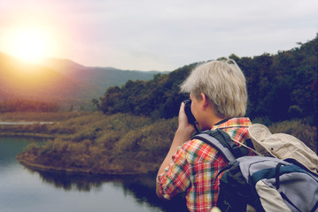 traveler man with backpack travel at mountain & lake. tourist backpacker use camera to take photo. lifestyle, summer vacation concept