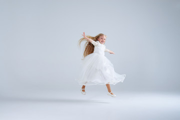 Fototapeta na wymiar Small girl wearing white dress jumping at studio