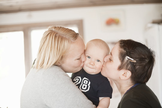 Two women kissing baby boy on cheeks