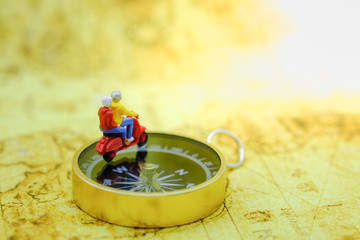 Travel and Tranport concept. Two traveler miniature figures ride motorcycle / scooter on compass...