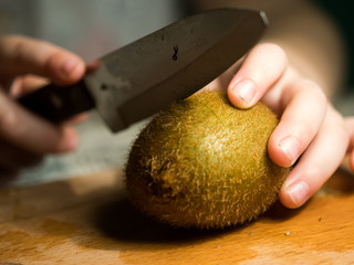 child cuts kiwi on a cutting board.
