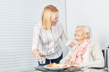 Junge Frau serviert Seniorin ein Mittagessen