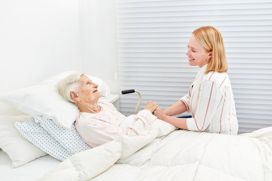 Frau macht Krankenbesuch bei bettlägeriger Seniorin