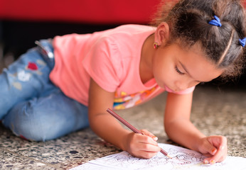 Obraz na płótnie Canvas Cute multiracial small girl drawing on a coloring book
