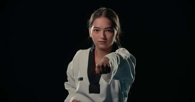 Asian beautiful girl a Taekwondo fighter performs punches in slow motion, dressed in a kimono, black background,