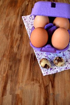 Chicken and quail eggs in a carton box on a wooden table