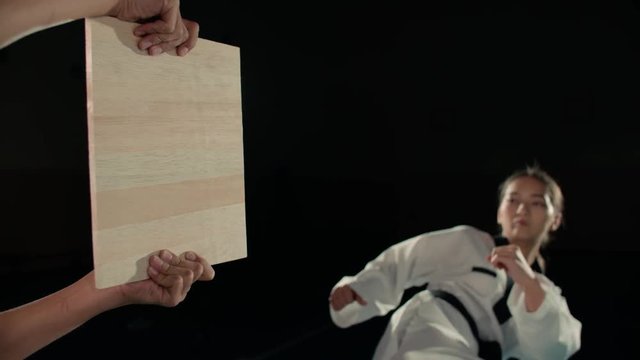 Asian beautiful girl fighter practicing to break the board with a blow to the hand, taekwondo in slow motion