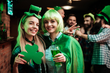 Two girls in a wig and a cap are photographed in a bar.