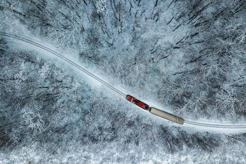 Budapest, Hungary - Aerial view of snowy forest with red train on a track at winter time, captured from above with a drone at Huvosvolgy - obrazy, fototapety, plakaty