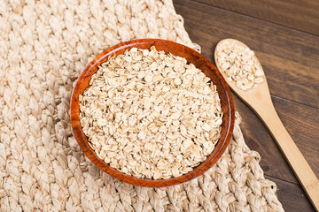 Bowl with oats next to wooden spoon on wooden table. Closeup