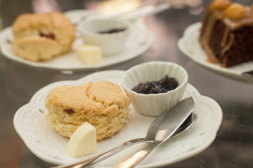 Butter scone with jam on white plate with butter knife and blur chocolate cake background.