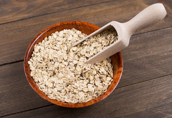Bowl with oats next to wooden spoon on wooden table. Closeup