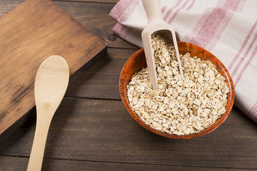 Oat flakes over bowl next to wooden spoon and wheat flower. Food