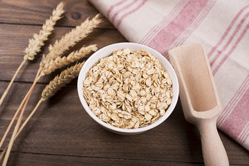 Oat flakes in a bowl next to wooden spoon and wheat flower.