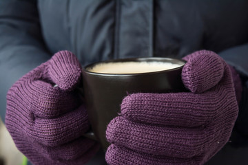 Male hands in violet gloves holding a cup with hot drink