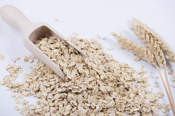 Oat flakes next to wooden spoon on white background. Isolated.