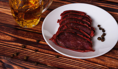 Fresh basturma on a white plate with a glass of beer on a wooden background