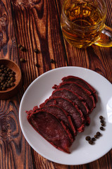 Fresh basturma on a white plate with a glass of beer on a wooden background