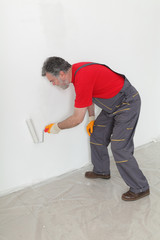Adult worker painting wall to white with paint roller