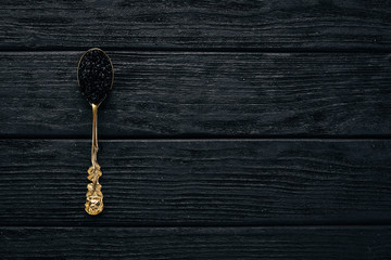 Spoon with black caviar on a wooden background. Top view. Free space for text.