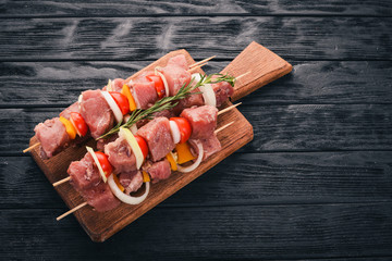 Raw kebab from meat on a wooden background with vegetables. Top view. Free space for text.